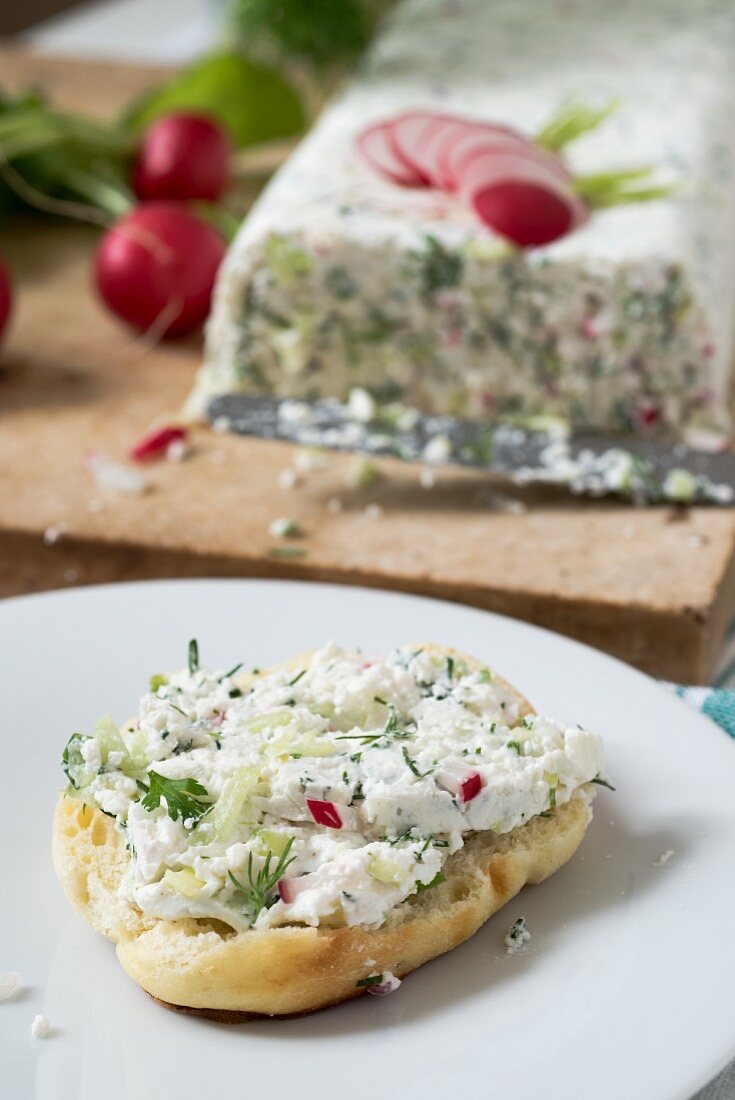 Half of a roll with quark cheese and herbs terrine spread on a white plate