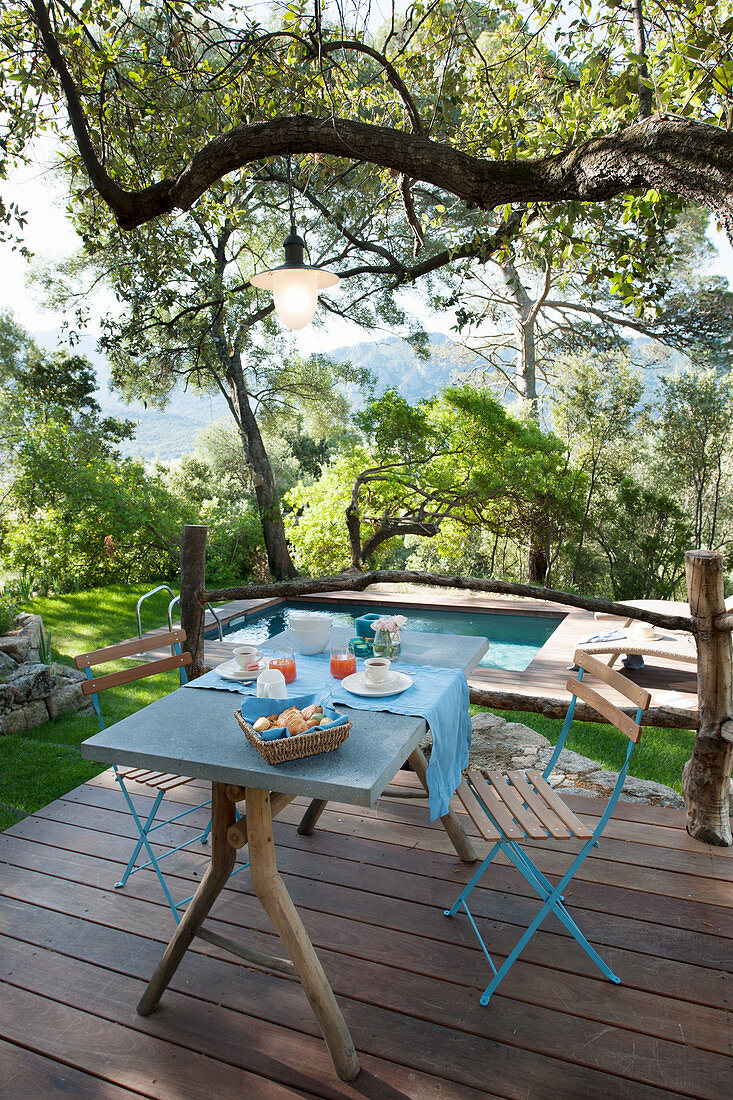 Set breakfast table on wooden terrace with swimming pool in background