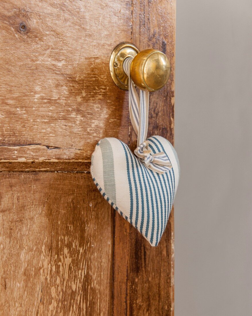 Blue and white striped fabric love-heart hung from knob of wooden door