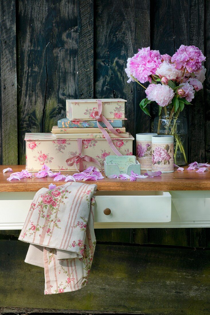 Romantic vintage-style still-life arrangement of peonies and decorative cardboard boxes against rustic board wall