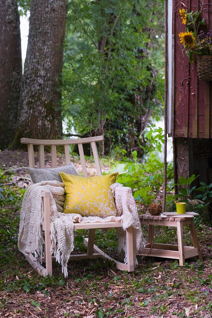 Gemütlicher Holzschaukelstuhl mit Kissen und Plaid vor Holzhütte