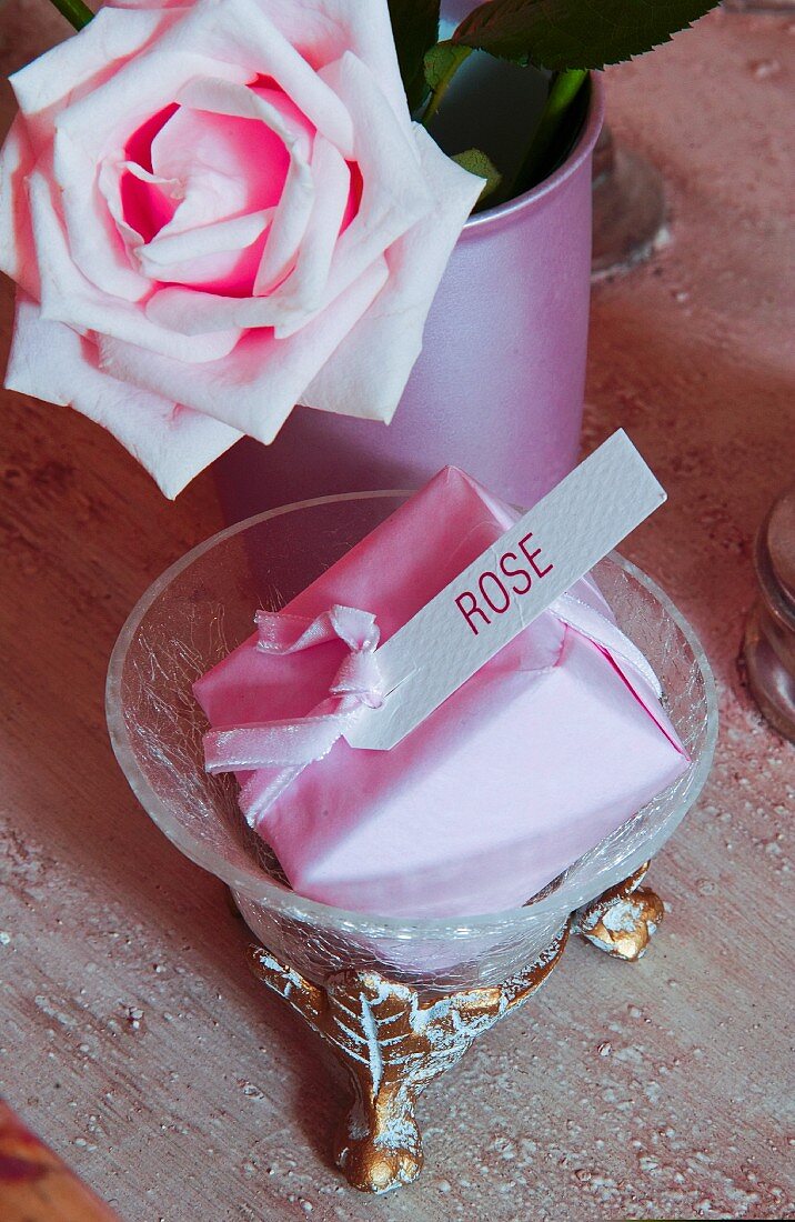 Soap wrapped in pink paper with label next to rose