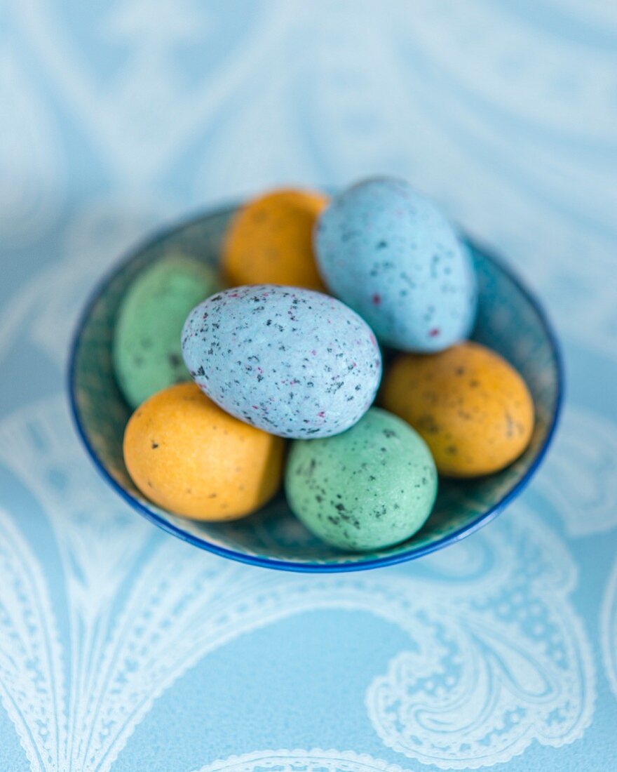 Colourful speckled eggs in bowl on pale blue tablecloth