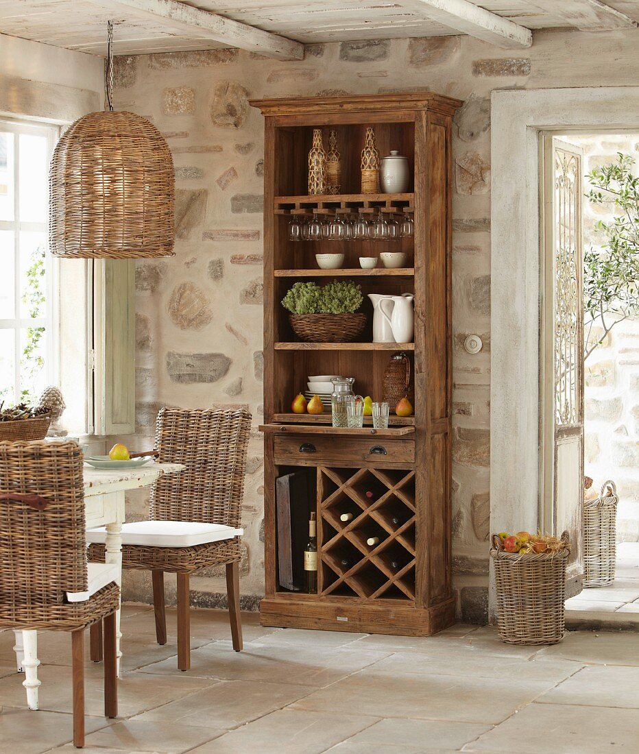 Crockery in cabinet with shelves and wine rack against stone wall in rustic dining area