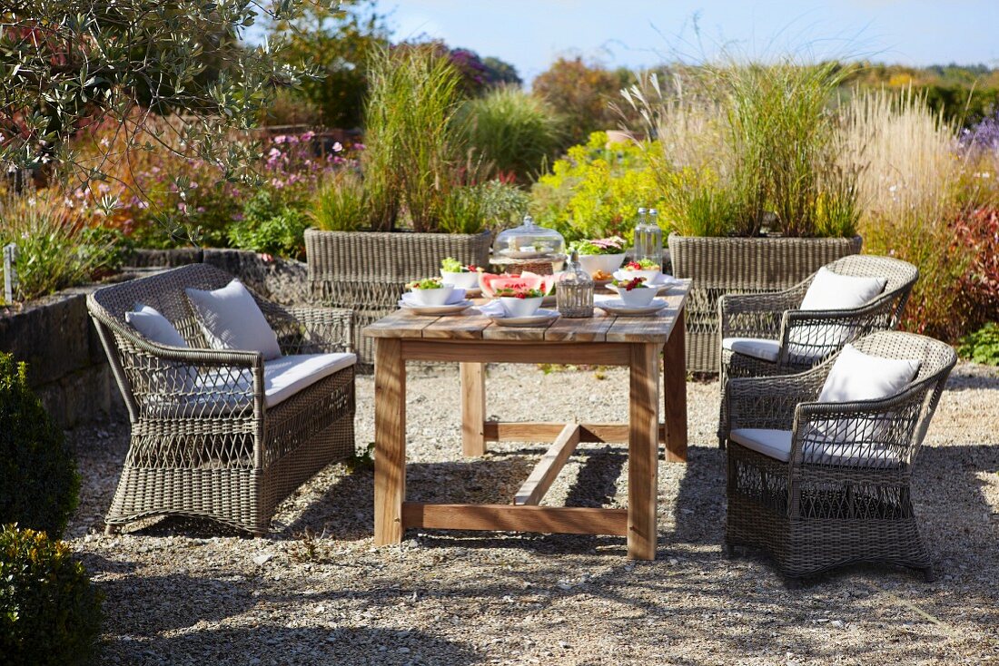 Terrassenplatz mit gedecktem Holztisch und Rattanmöbeln vor sommerlichem Garten