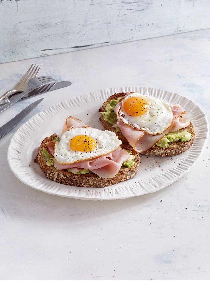Two slices of bread topped with ham, fried egg and avocado