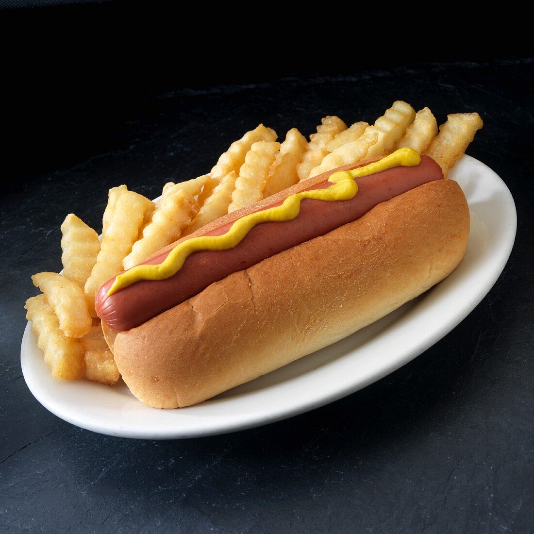 Hot dog with yellow mustard and french fried potatoes