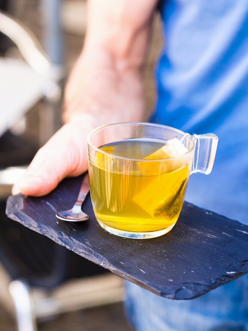 Person serviert eine Tasse Grüntee auf Schieferplatte