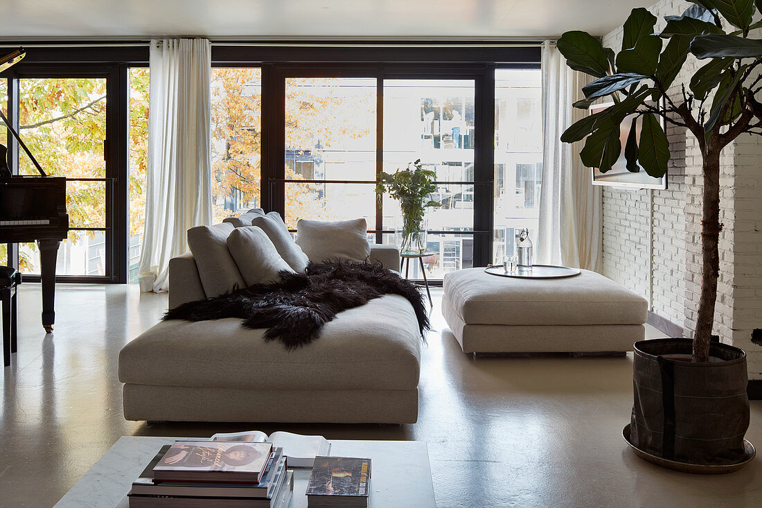 Sofa and ottoman in loft apartment with concrete floor and glass wall