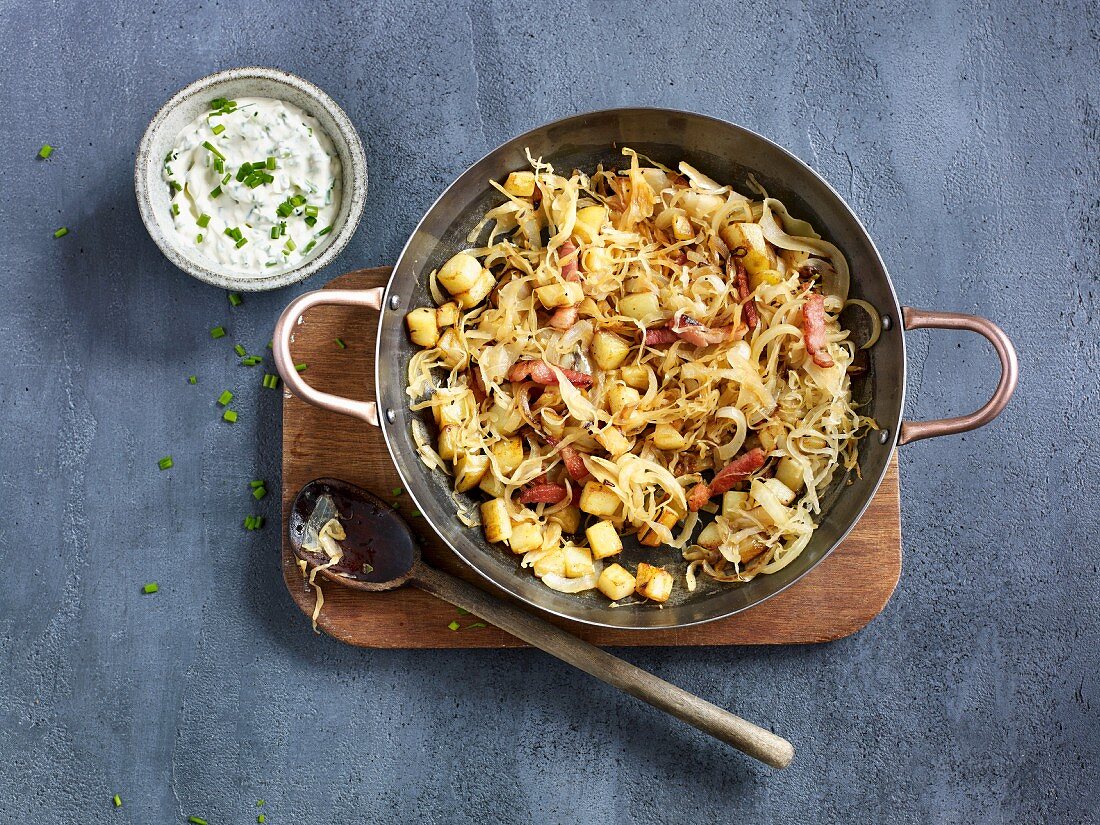 Fried potatoes and sauerkraut in a pan served with a creamy chive dip