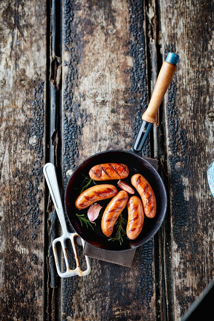 A frying pan with sausages, garlic and rosemary