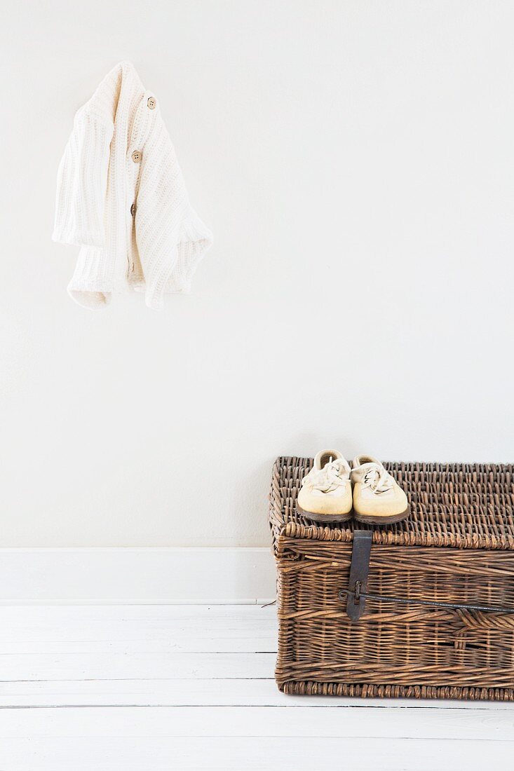 Cardigan hung on wall above white shoes on wicker trunk