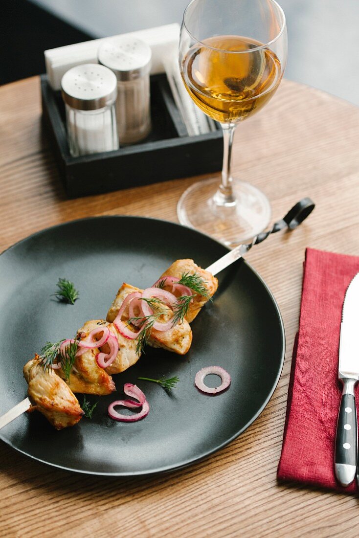 A chicken skewer with red onions and dill on a black plate