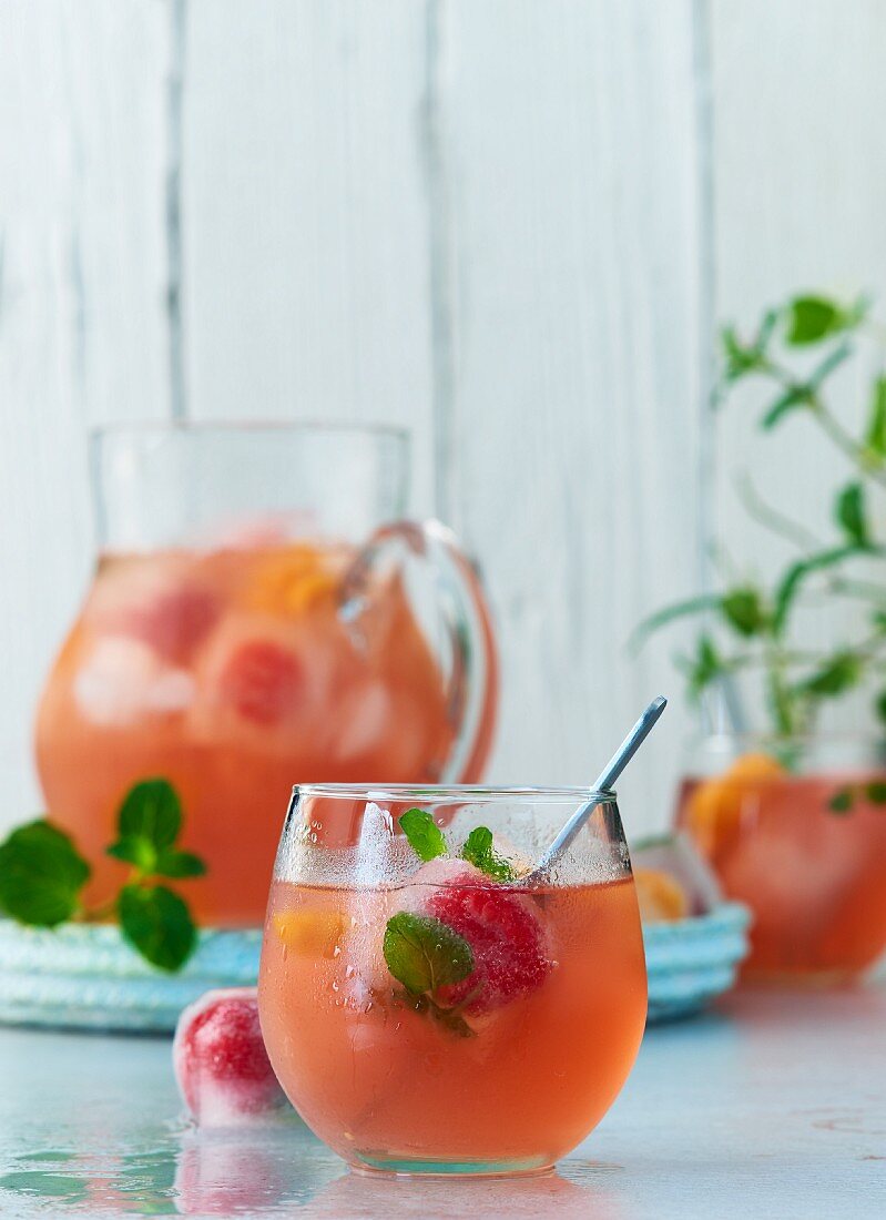 Fruchtige Sommerbowle mit Granatapfelsaft, Mineralwasser, Minze und Eiswürfeln mit eingefrorenen Beeren