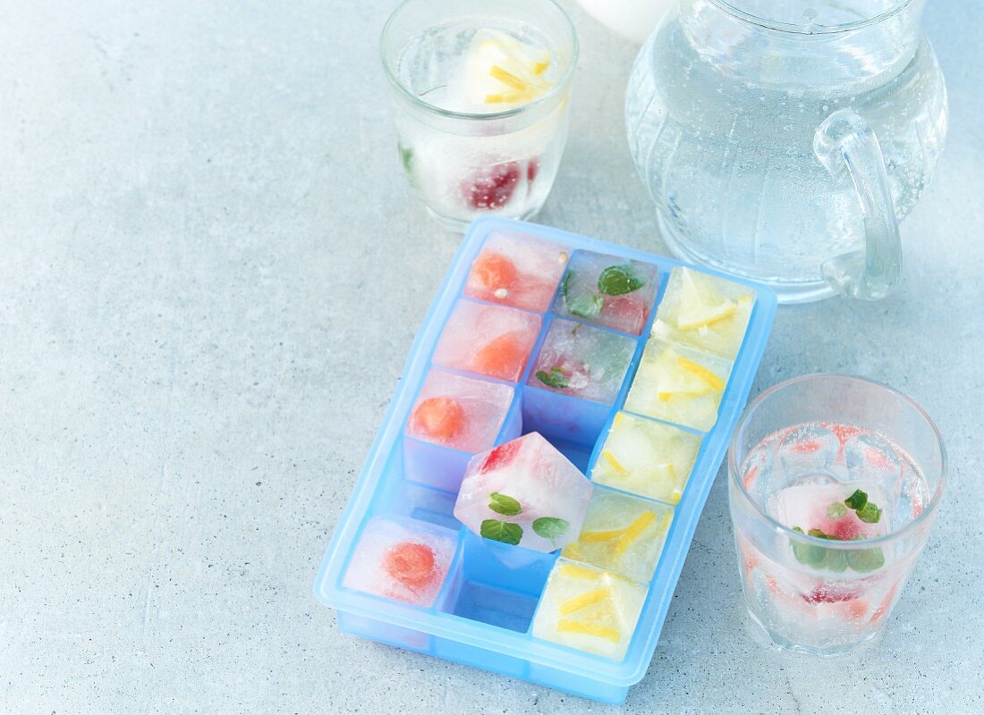 Sommerliche Fruchteiswürfel in Eiswürfelbehälter und in Gläsern