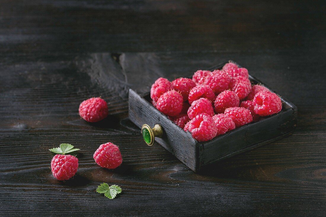 Fresh organic wet ripe raspberries in black wood box over wooden burnt background