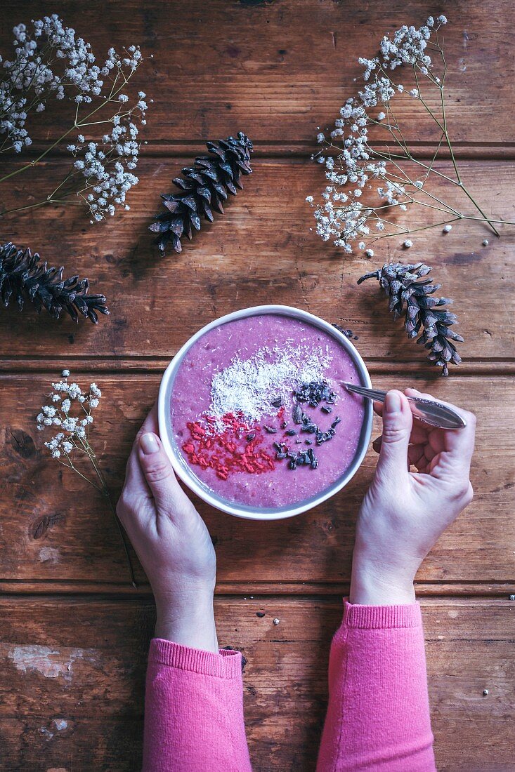Woman eating raspberry smoothie bowl on a rustic wooden table