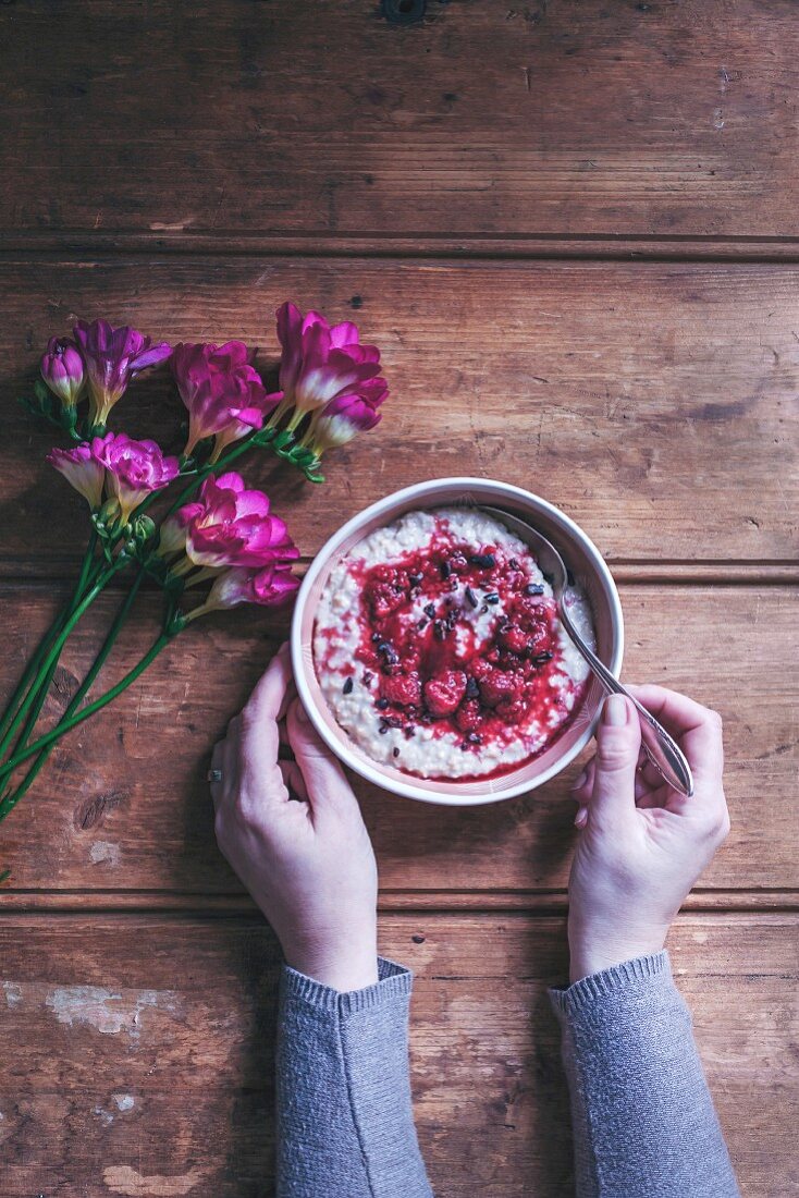 Woman eating porridge with raspberry sauce and cacao nibs in a bowl