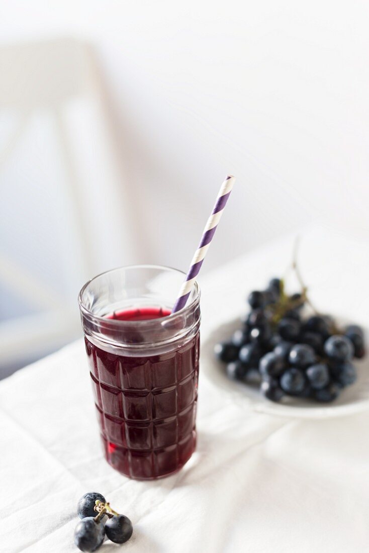 Red grape juice in a glass with a straw