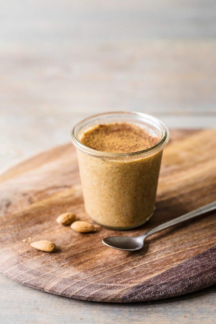 Jar of almond and cinnamon butter on a wooden tray with a few whole almonds and a spoon