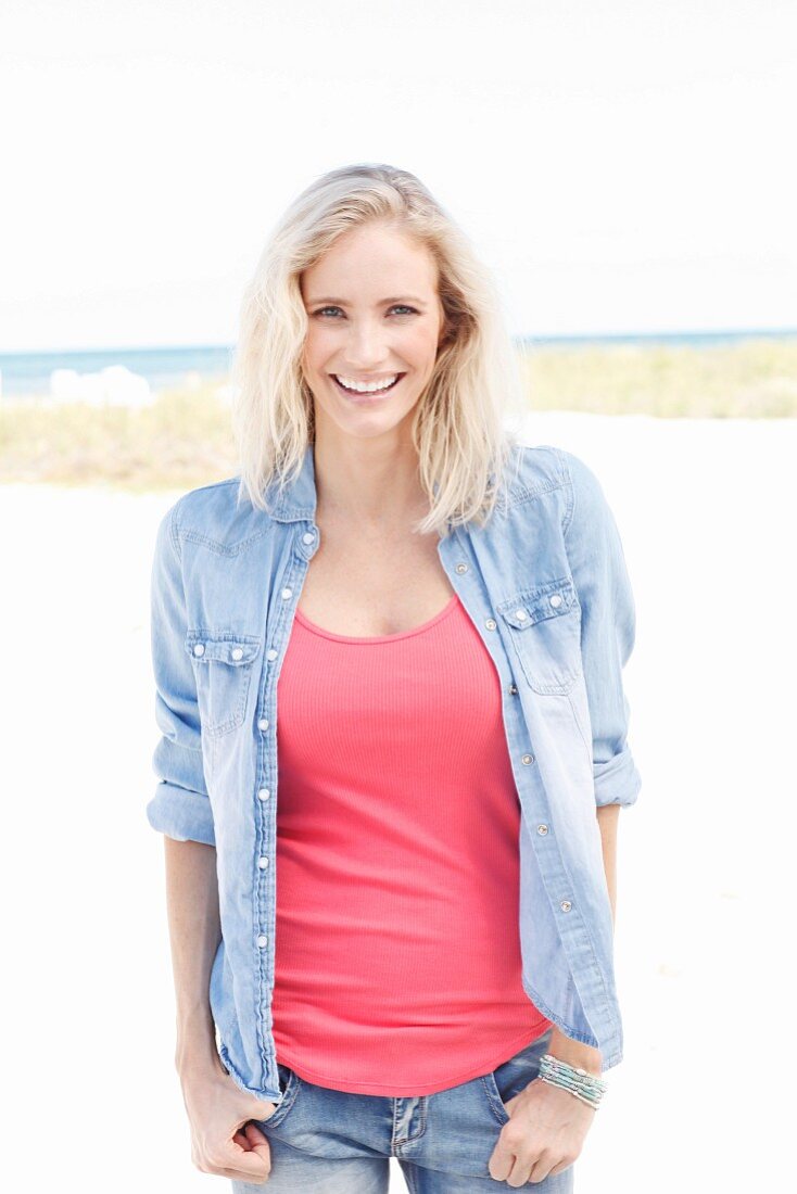 A blonde woman wearing a pink top, a denim shirt and jeans