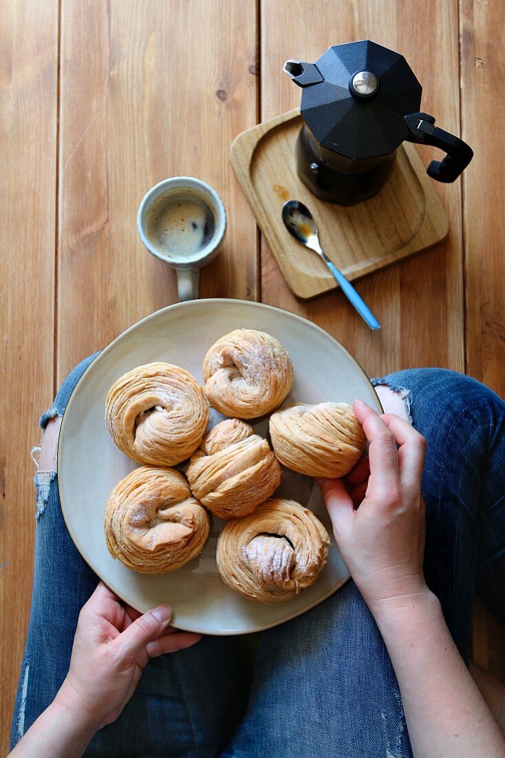 Female sitting on the floor and having breakfast with cruffin pastry and a cup of coffee