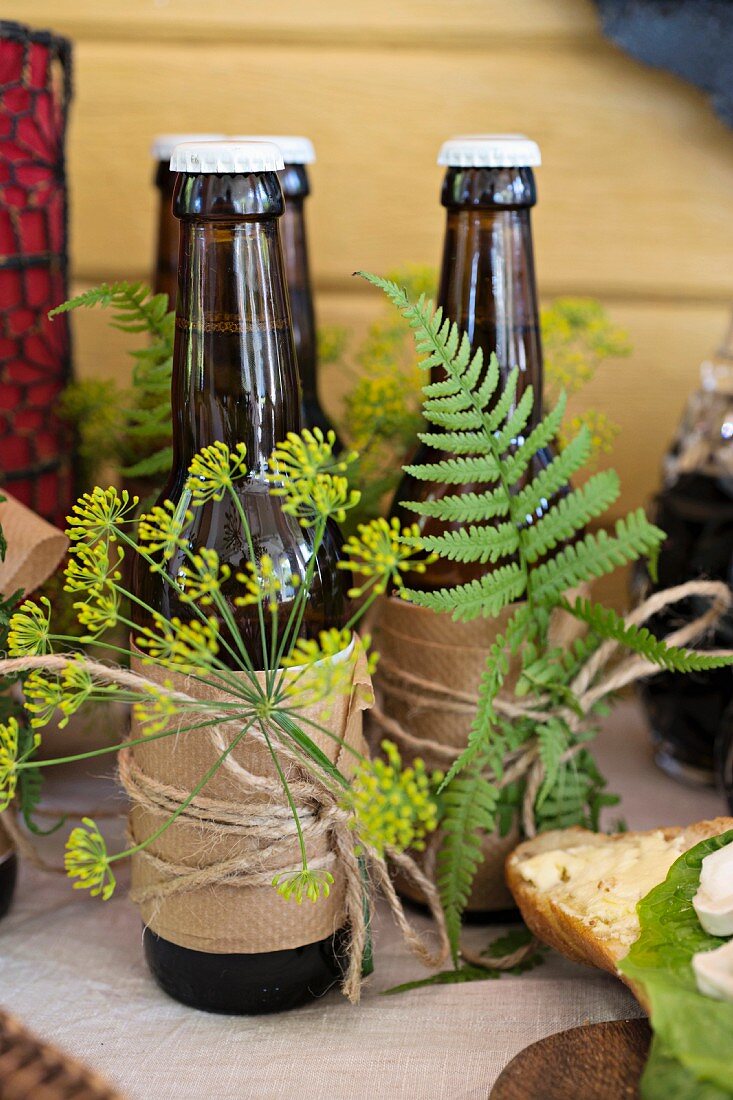 Bottles of beer wrapped in paper and decorated with dill flowers and ferns on dresser