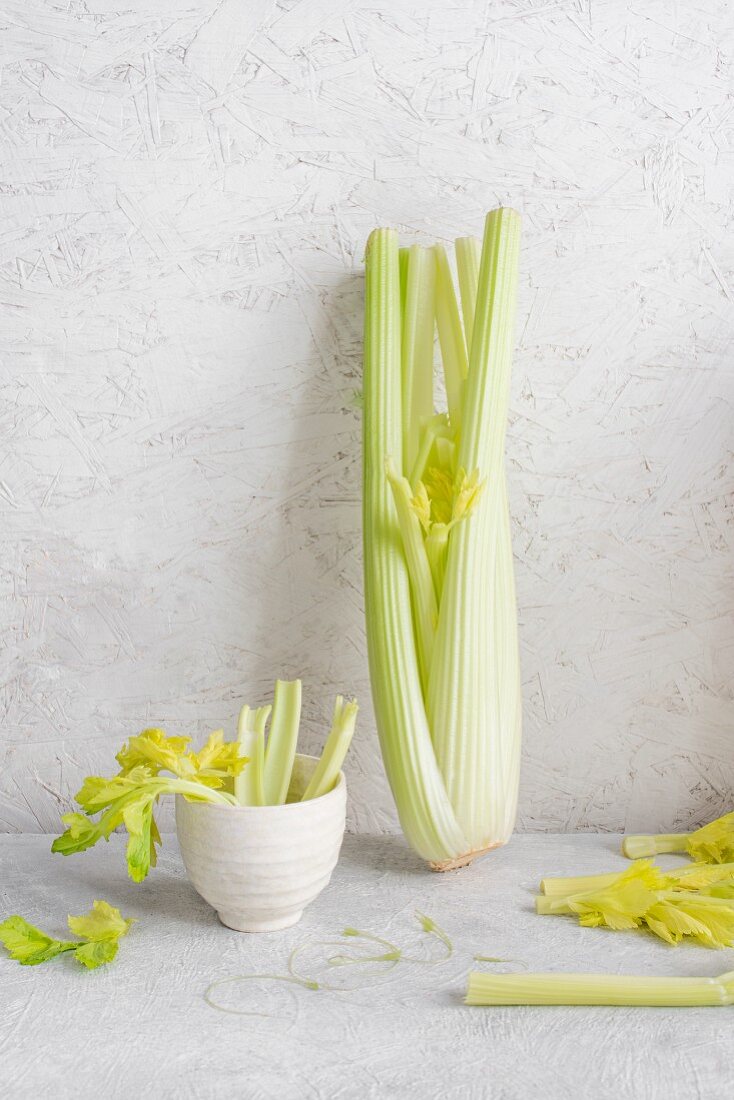 A whole celery plant and celery stalks in small bowls