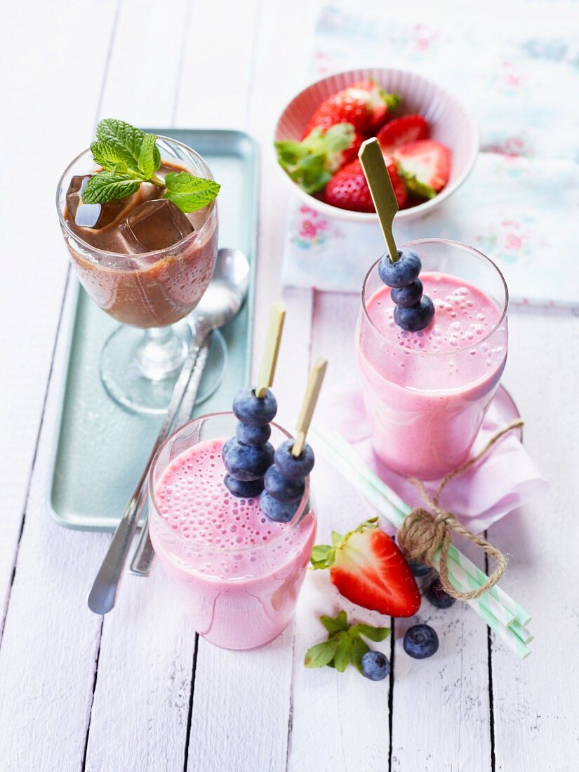 A coffee shake with ice cubes and two strawberry shakes with blueberry skewers