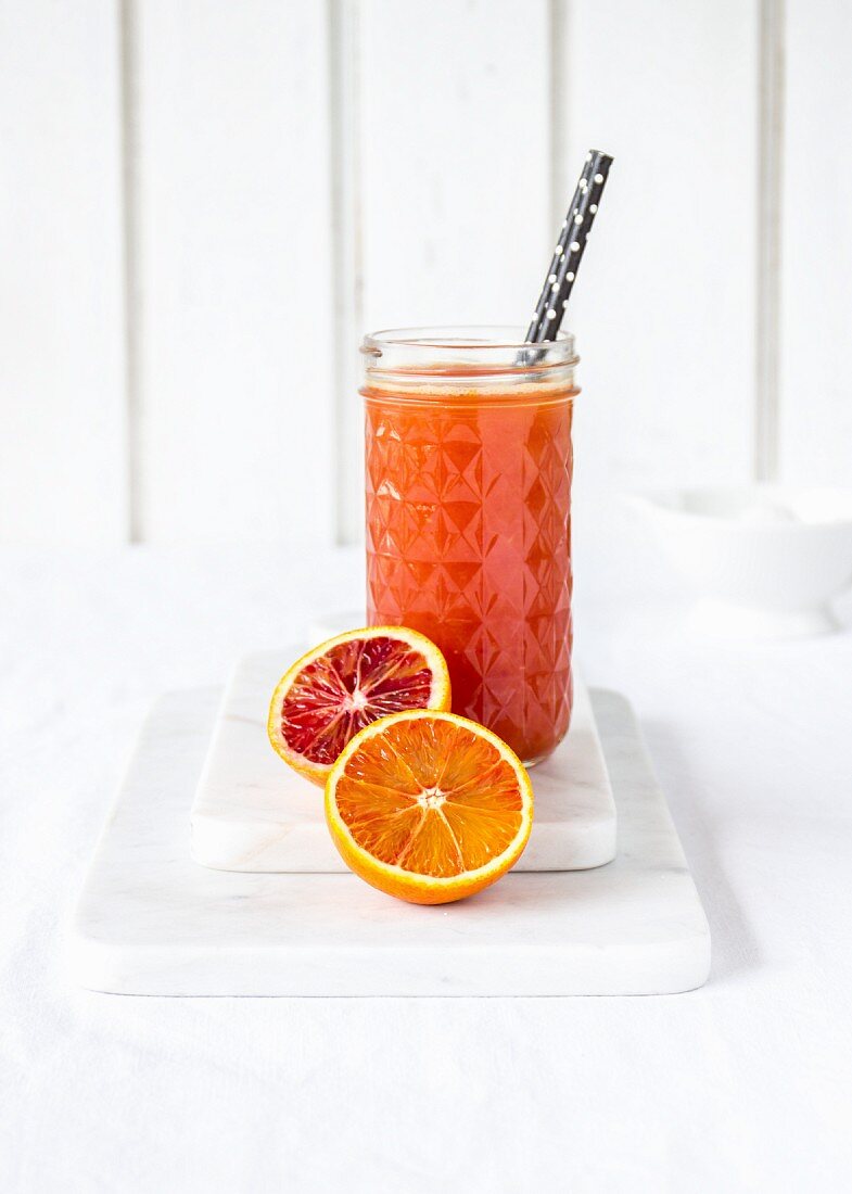 Freshly squeezed blood orange juice in a glass with a drinking straw
