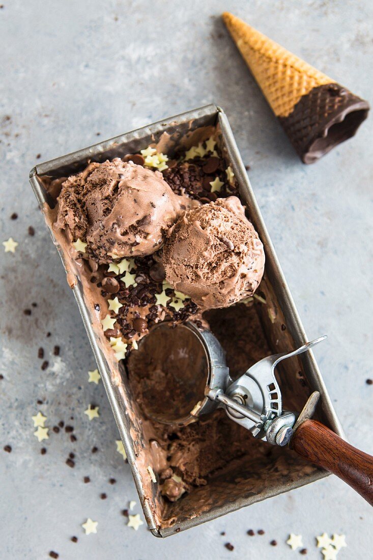 Triple Schokoladeneis in einem Behälter, Eisportionierer und Waffeltüte