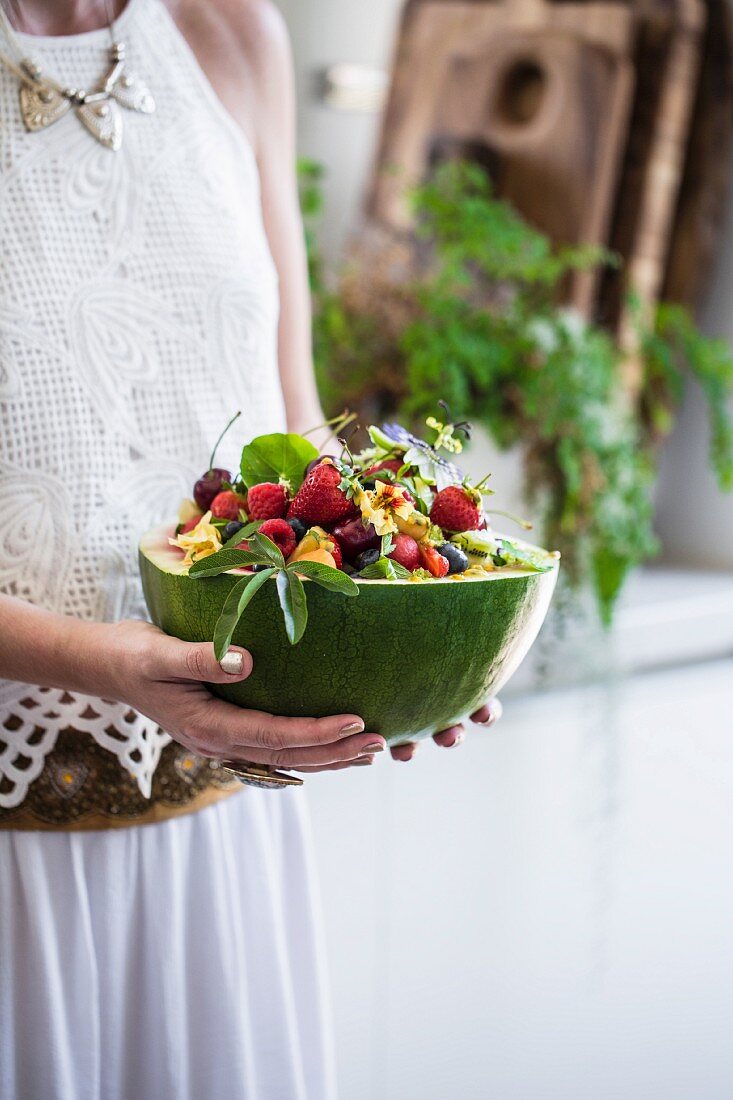 A woman holding a hollowed-out watermelon filled with a fruit salad