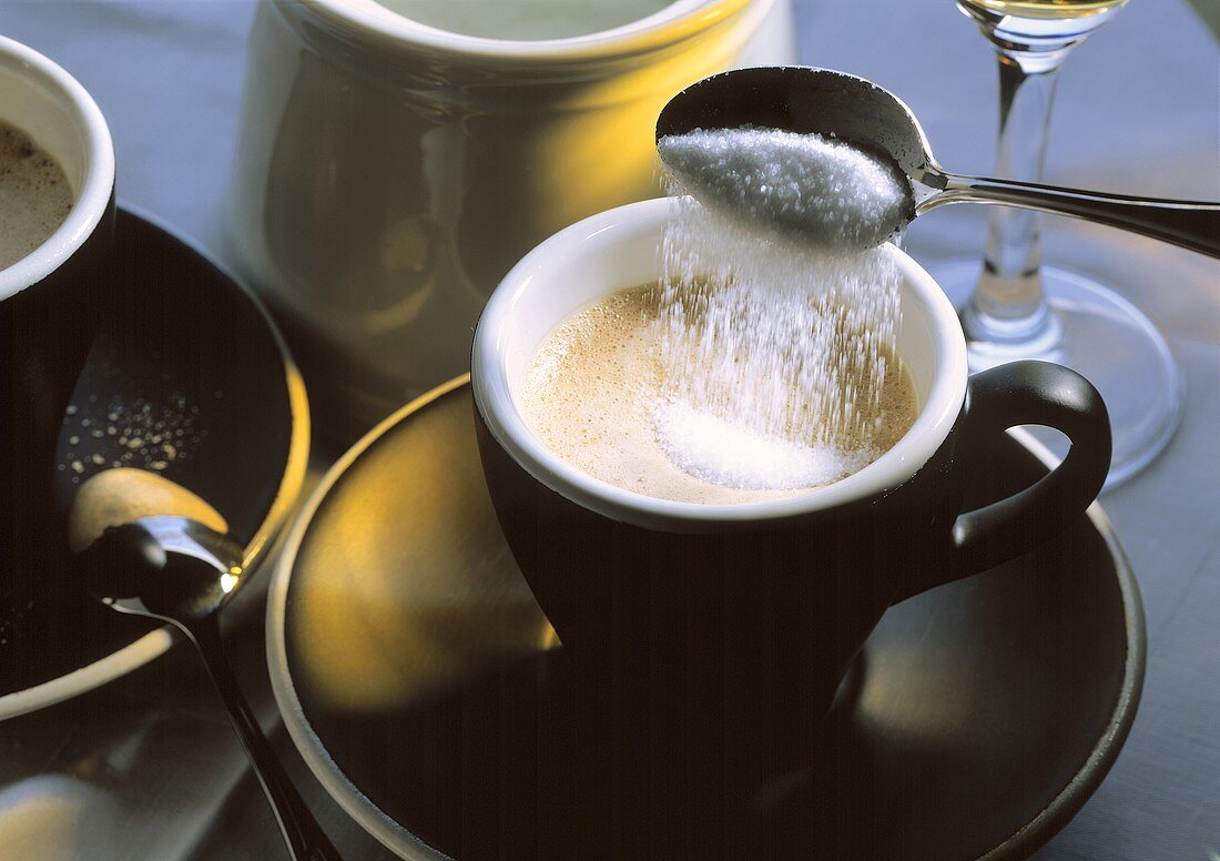 Ein Löffel Zucker wird in Cappuccino geschüttet