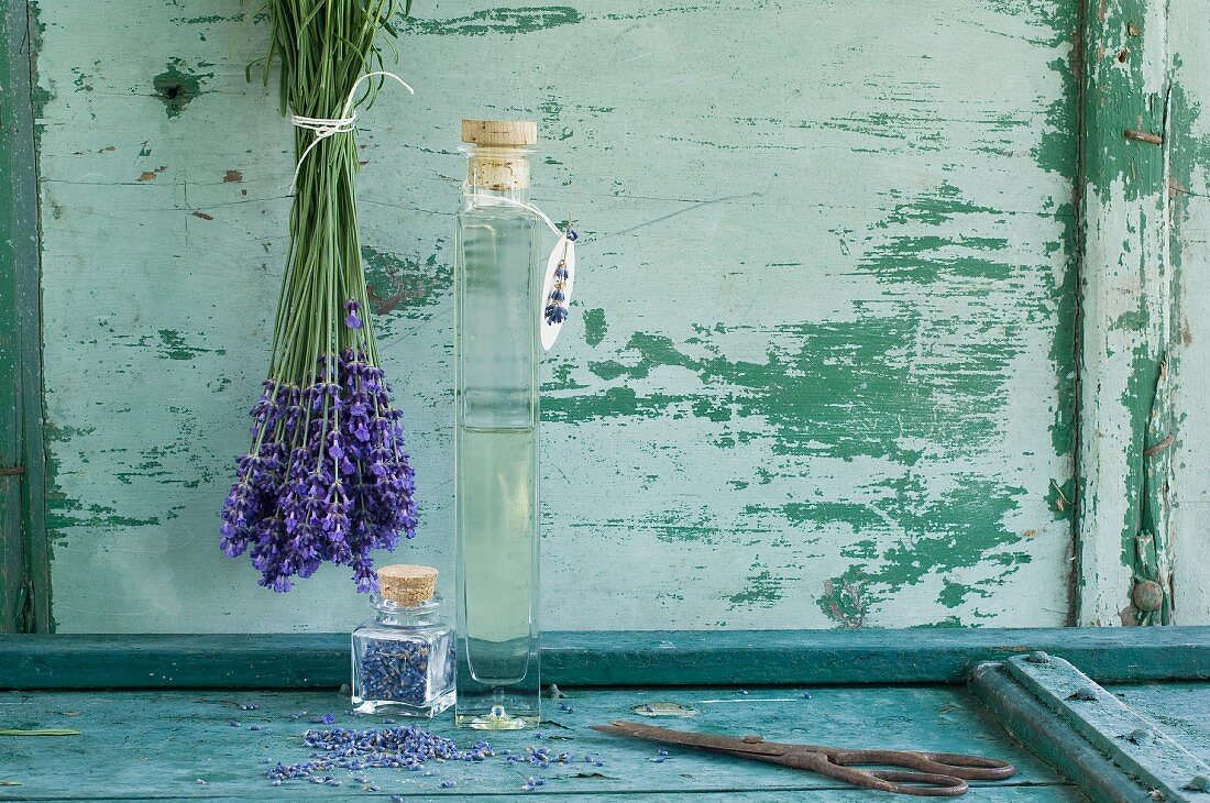 Lavendelöl in einer Glasflasche, Lavendelstrauß und getrocknete Lavendelblüten in einem Glasbehälter