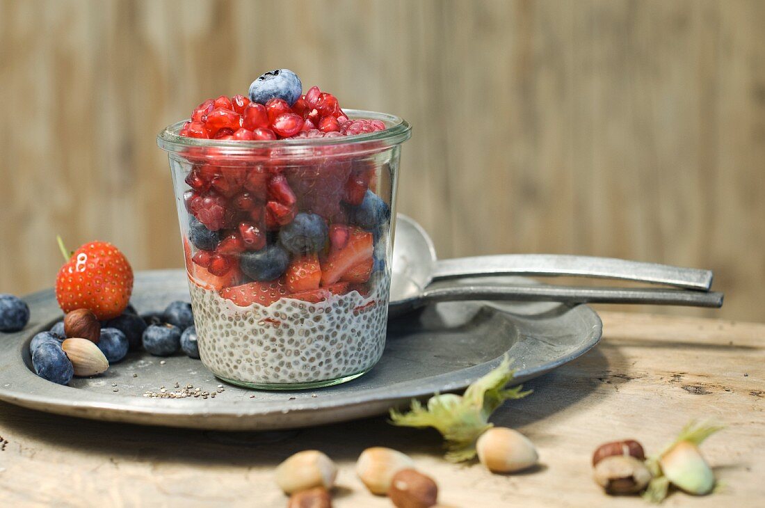 Glasses of chia pudding with different berries, pomegranate seeds and hazelnuts