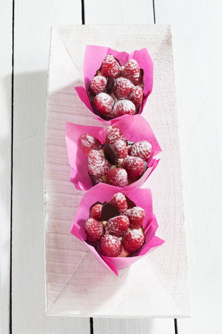 Drei Himbeeren Muffins in rosa Papiermanschetten