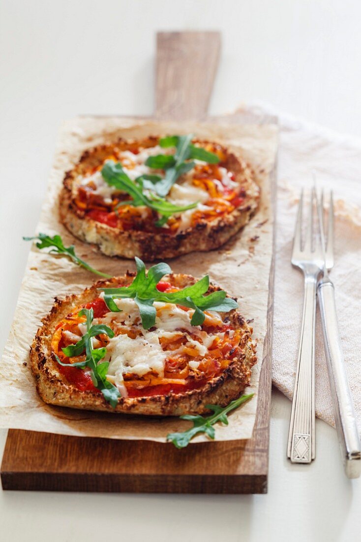 Two homemade glutenfree mini pizzas with cauliflower, pumpkin and rocket on wooden board