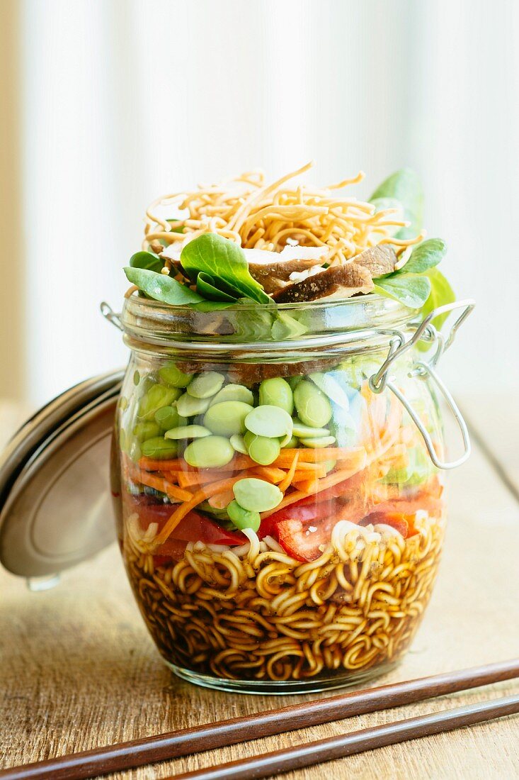 Asian salad in a jar with ramen noodles, red pepper, snow pea pods, carrots, edamame, shiitake mushrooms, salad greens, fried chow mien noodles and dressing