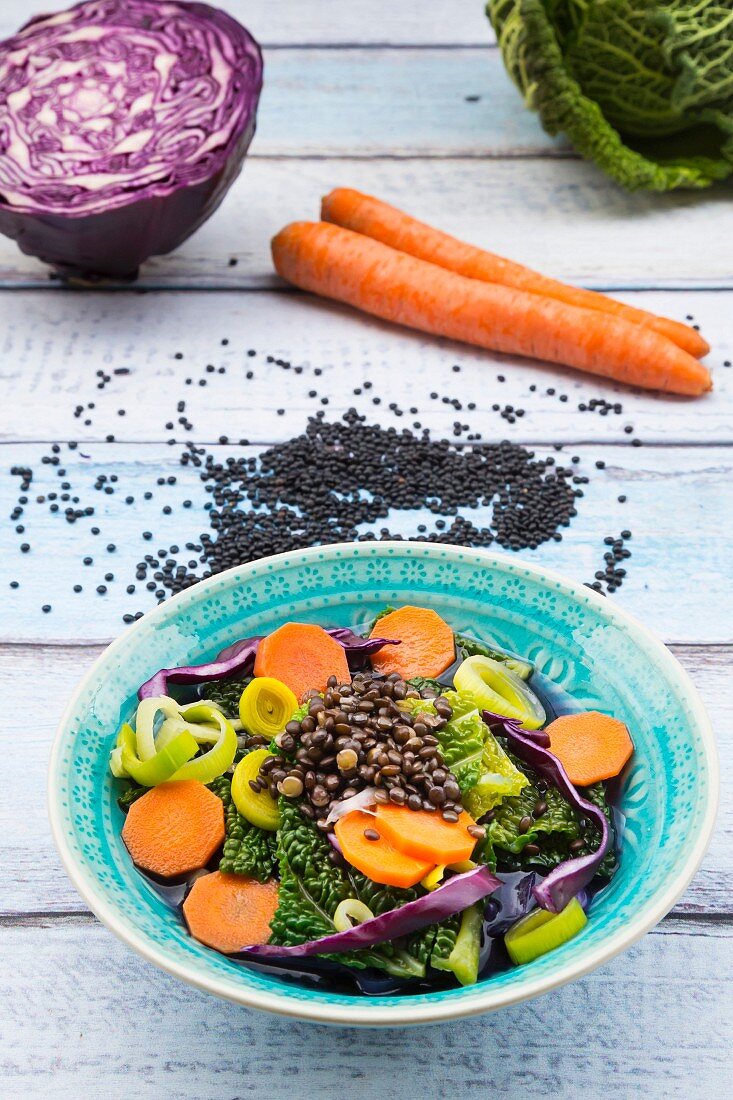 Bowl of vegan cabbage stew with lentils and ingredients on wood