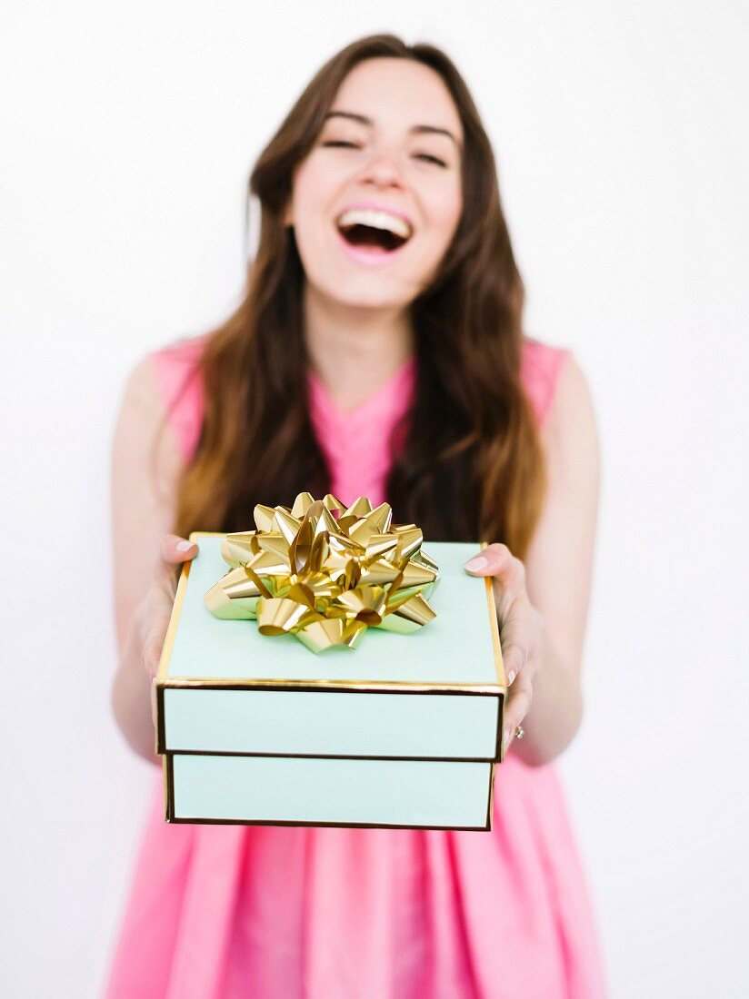 A brunette woman wearing a pink dress and holding a gift box in her hands