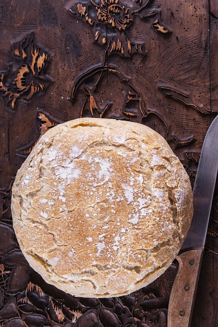 Wheat bread baked in a pot: a whole loaf on a wooden surface (top view)