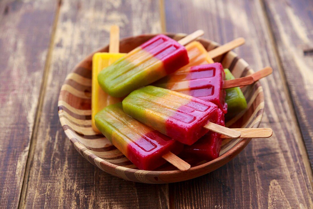 Wooden bowl of homemade fruit smoothie ice lollies on wood