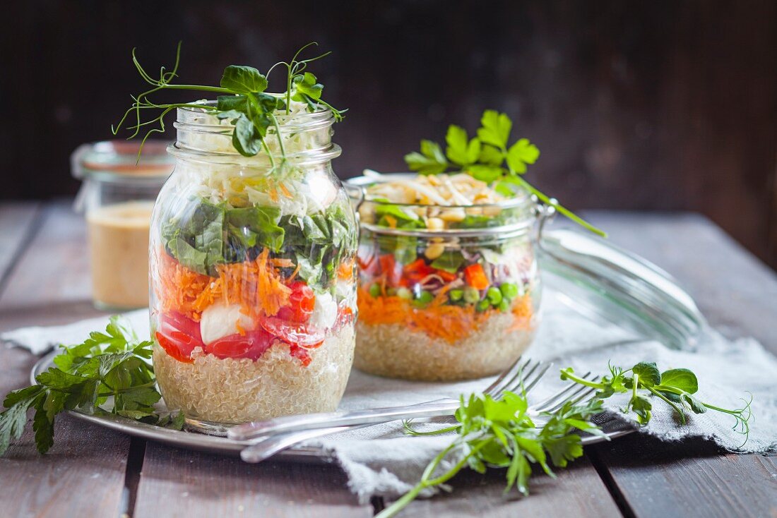 Rainbow salads in jars, quinoa, carrots, peas, red cabbage, bell pepper, mung bean sprouts, the other with tomatoes, mozzarella, spinach, pea sprouts