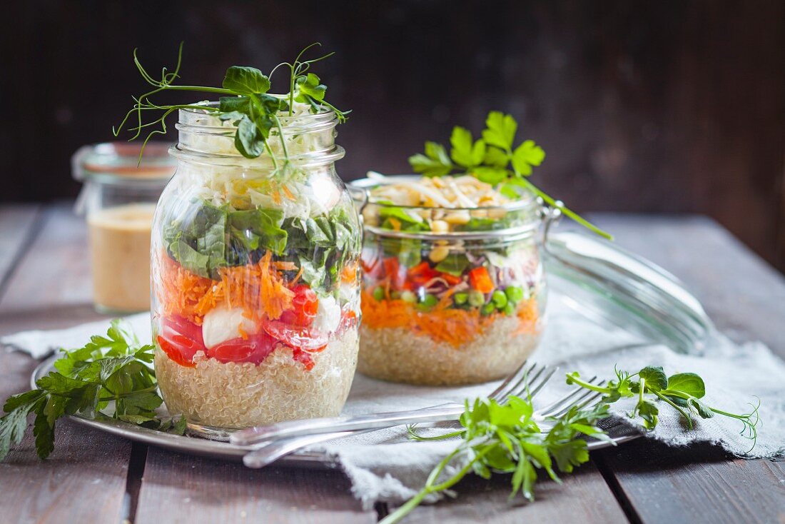 Regenbogen-Salate in Gläsern (Quinoa, Karotten, Erbsen, Rotkohl, Paprika, Mungobohnensprossen und Tomaten, Mozzarella, Spinat, Erbsensprossen)