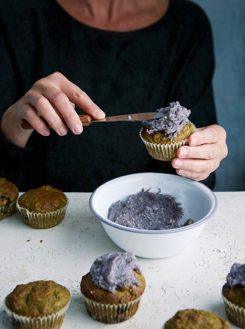 Frosting being spread onto green oat and blueberry muffins with a knife