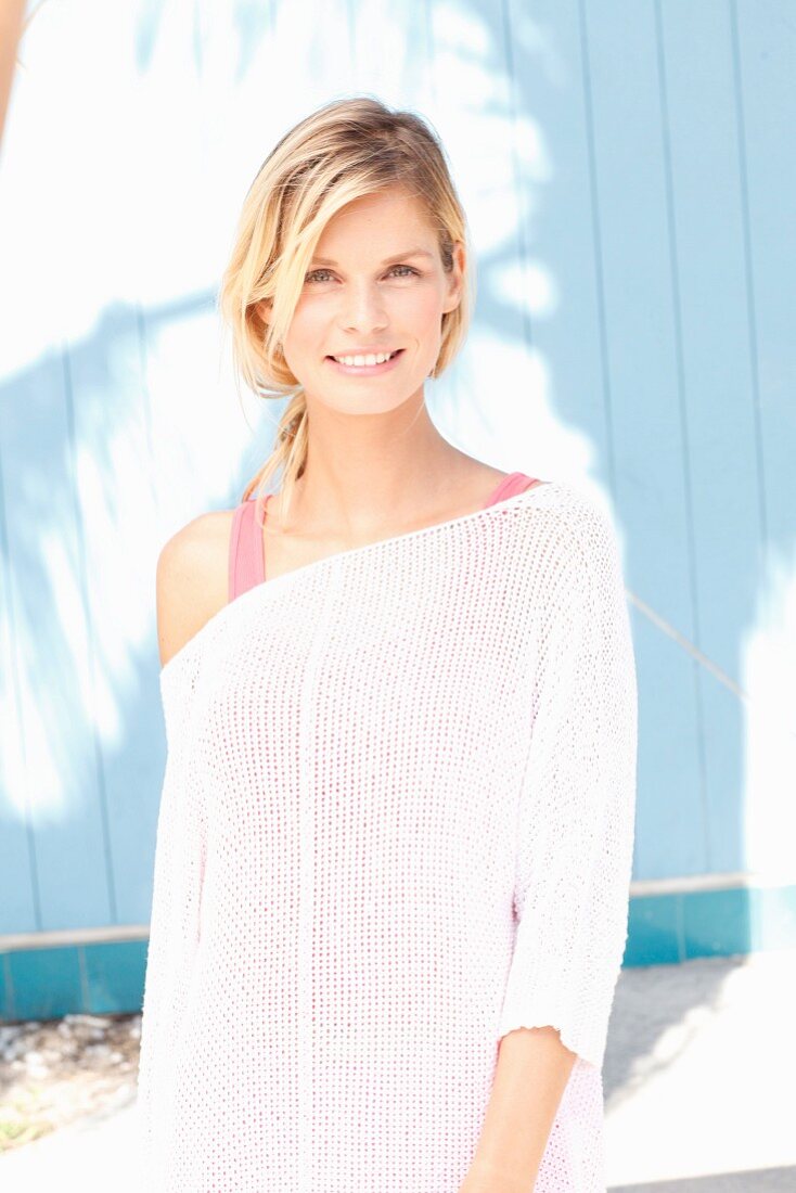 A blonde woman wearing a pink top and a white knitted jumper