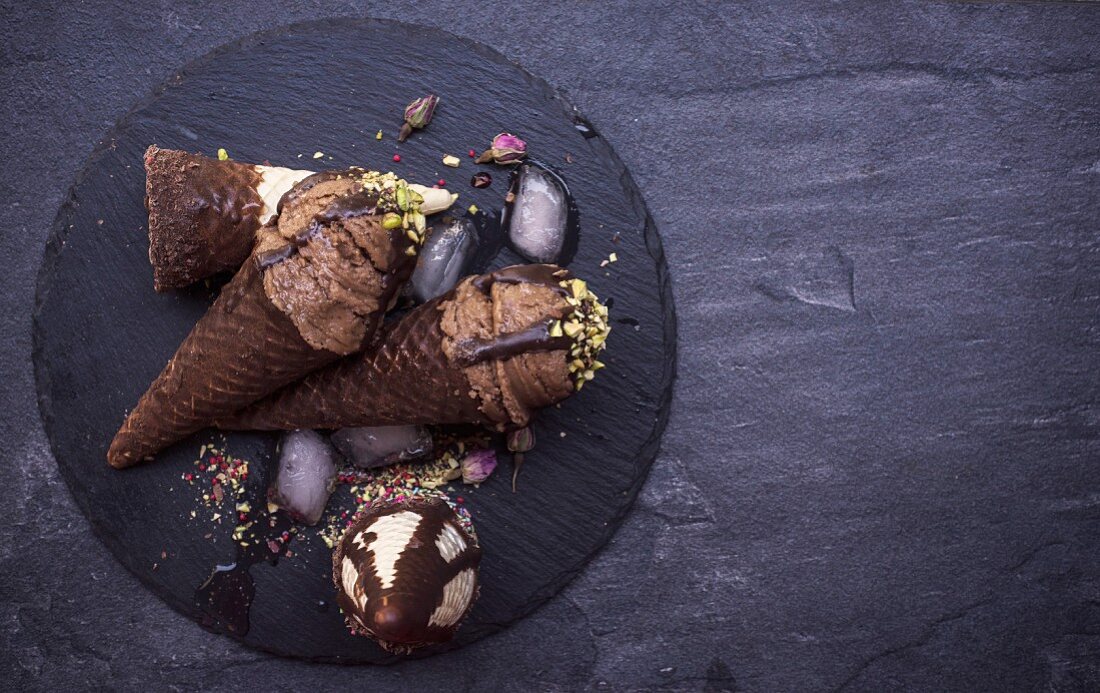 Schokoladeneis mit Pistazien in Waffeltüten auf schwarzem Teller