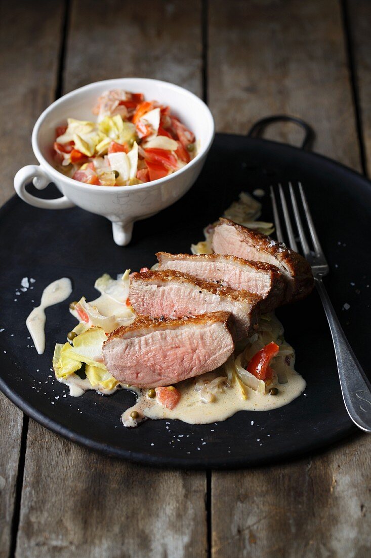 Fried duck breast on a bed on chicory and tomato sauce