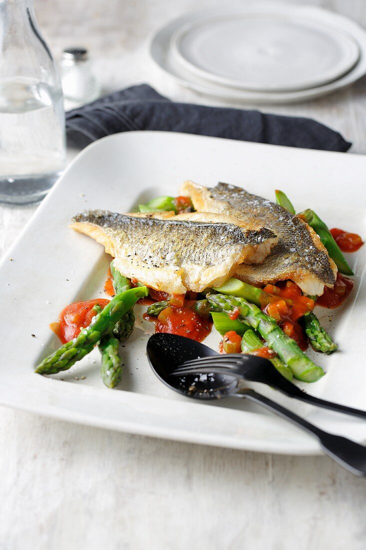 Fried gilthead bream fillets on a bed of green asparagus with tomato sauce