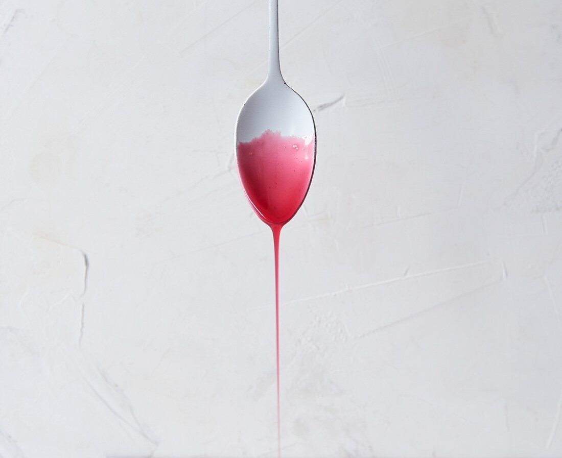 Red sugar syrup dripping from a tablespoon